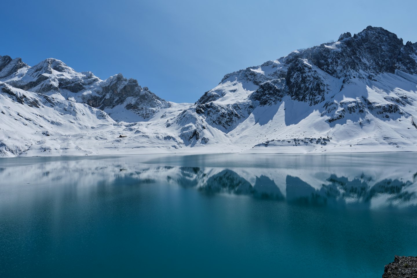 Snow-capped mountains reflect in the clear water of an alpine lake.