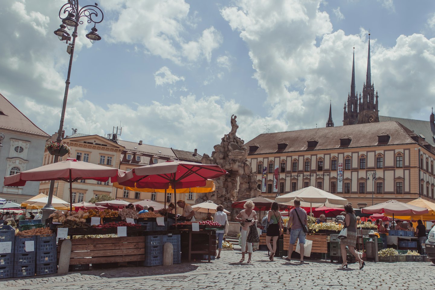 Shoppers browse produce stalls in a historic European town square.