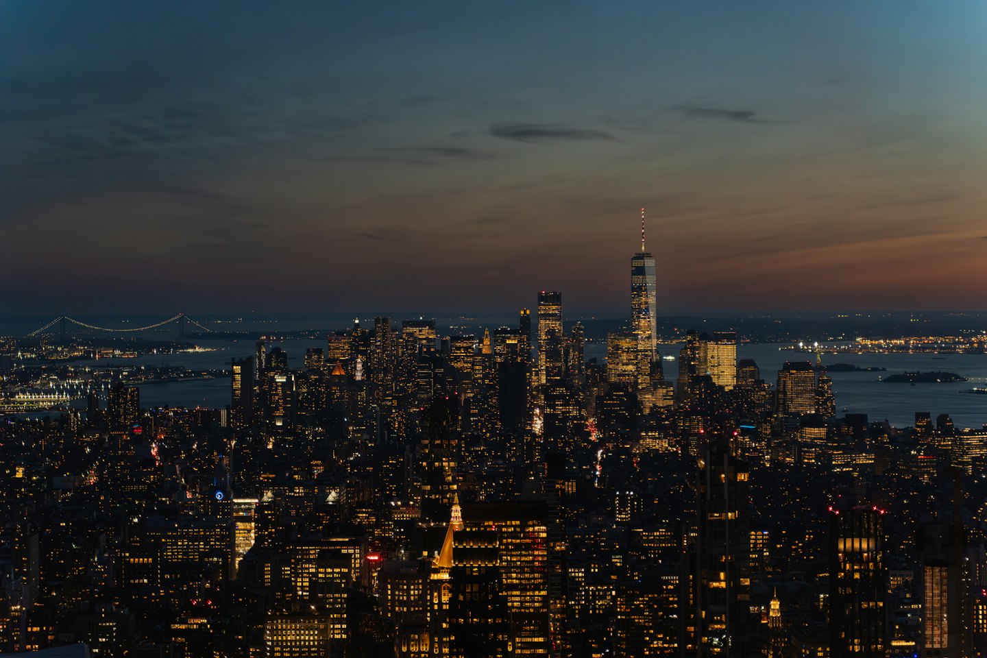 Illuminated skyscrapers line a dense city skyline at sunset.