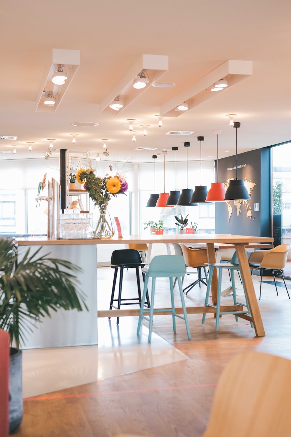 Modern office with communal table, colorful stools, and world map wall art.