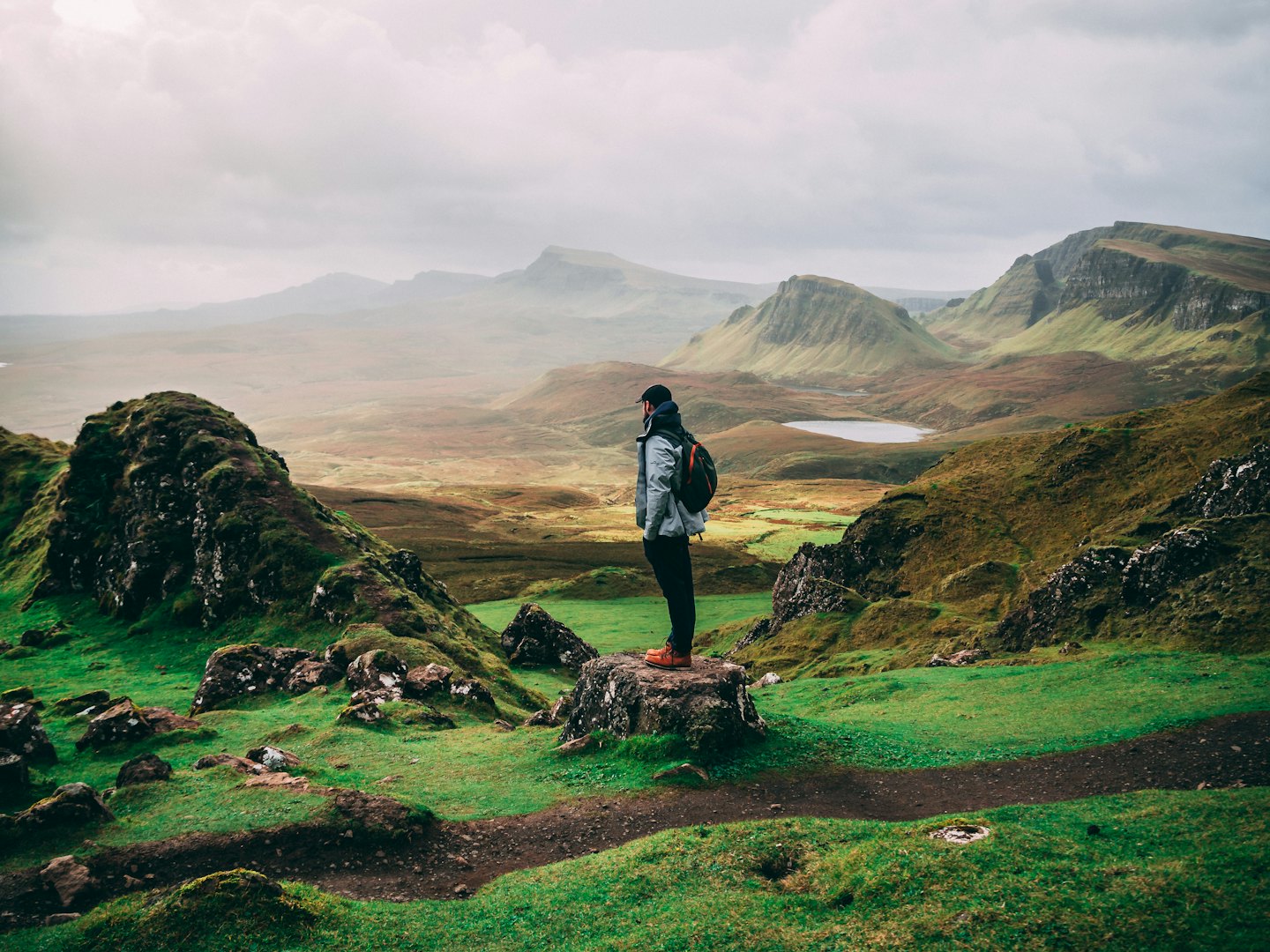 Hiker with a backpack stands on a rocky mountain ledge.